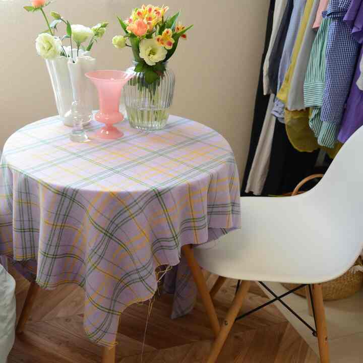 Pastel checkered tablecloth on round table in small room with white chair and floral vases, cozy cafe style ambience