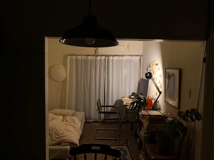 Darkly lit natural-toned single household bedroom and workspace with desk and bed