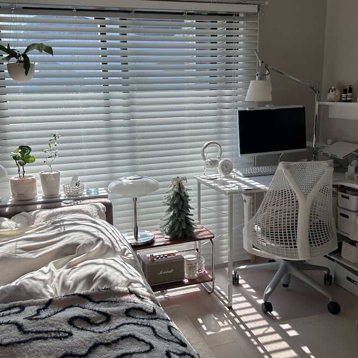 Bright white-toned bedroom and home office space featuring a white desk and chair, plants, and a clean modern interior