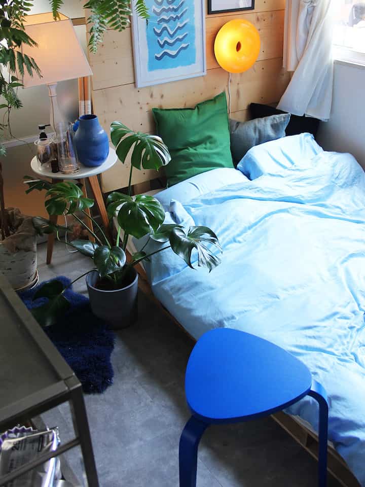 柔らかなブルーとグリーンが調和する寝室、木目調の壁と植物が自然な雰囲気を作るインテリア