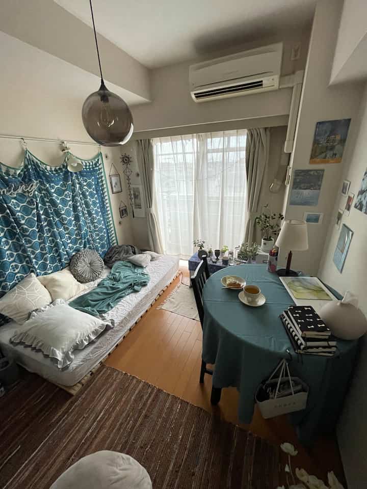 ナチュラルな色調の小さな一人暮らし用の部屋、中央に丸いダイニングテーブルとソファベッドが配置された印象的な空間