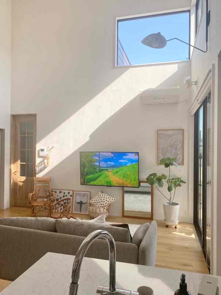 Natural wood floor and white walls define the living room with rattan chairs and large windows creating a bright and cozy atmosphere