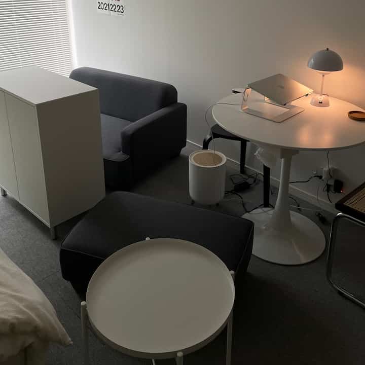 白とグレーの色調のモダンなリビング、ソファと丸いナイトテーブル、書斎机が整然と配置された空間