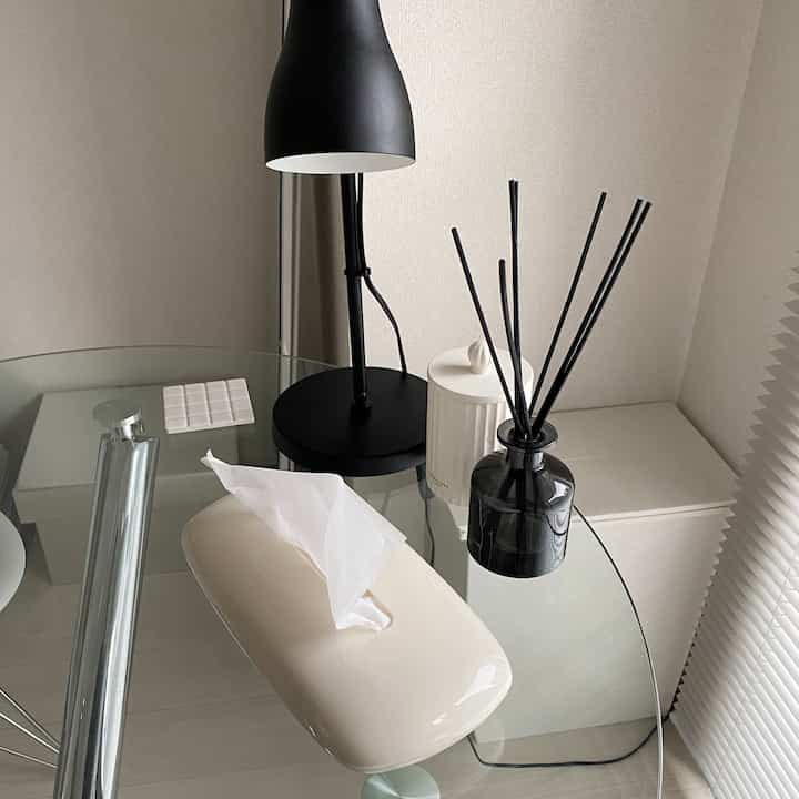 Modern living room in white and black tones featuring a transparent glass table with table lamp, diffuser, and candle decor.
