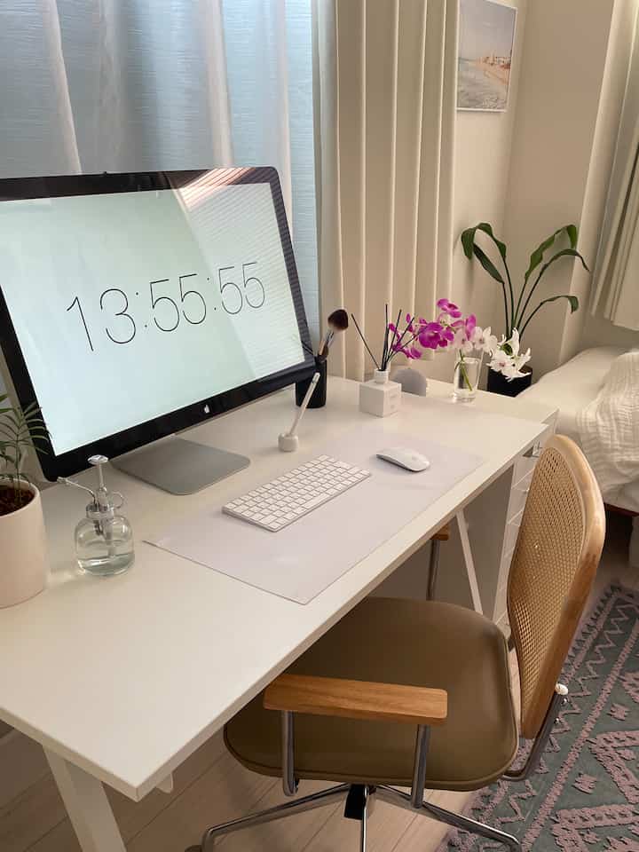 White-toned studio workspace featuring a neat desk, rattan chair, and plants creating a cozy atmosphere