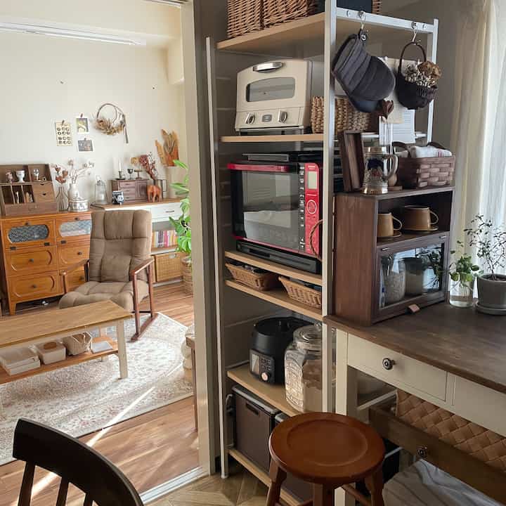 Bright and warm natural-toned living room and kitchen space featuring wooden furniture and organized storage shelves in a cozy setting