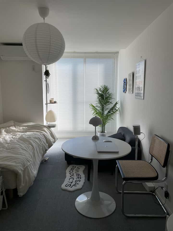 White and black toned studio apartment featuring a round table, sofa, floor lamp, and plant in a simple setting