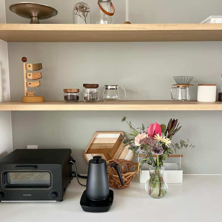 グレーの壁と木目調の棚があるキッチン、透明な花瓶にセピア色のアンスリウムの花束が置かれたシンプルで印象的な空間