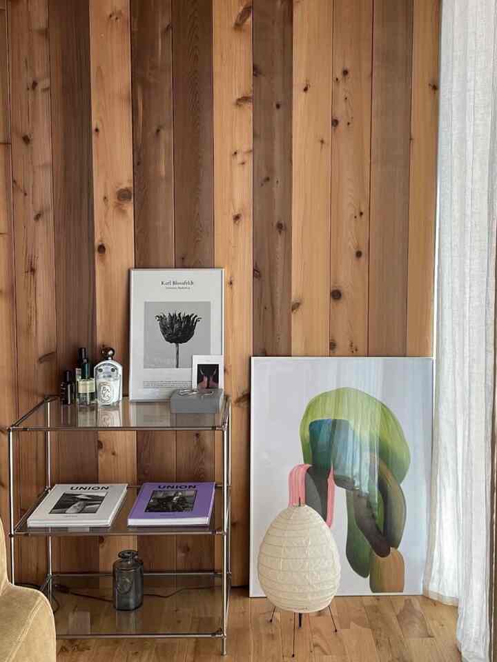 ナチュラルな木目調の壁と床が印象的なリビングのコーナー、メタルシェルフとフロアランプ、アートポスターが配置された雰囲気ある空間