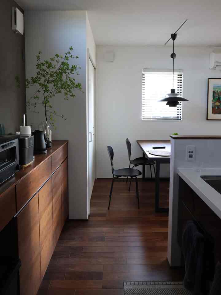 温かみのあるブラウンの木目調と白い壁が調和するモダンなキッチン・ダイニング、黒の椅子が2脚配置されている印象的な空間。