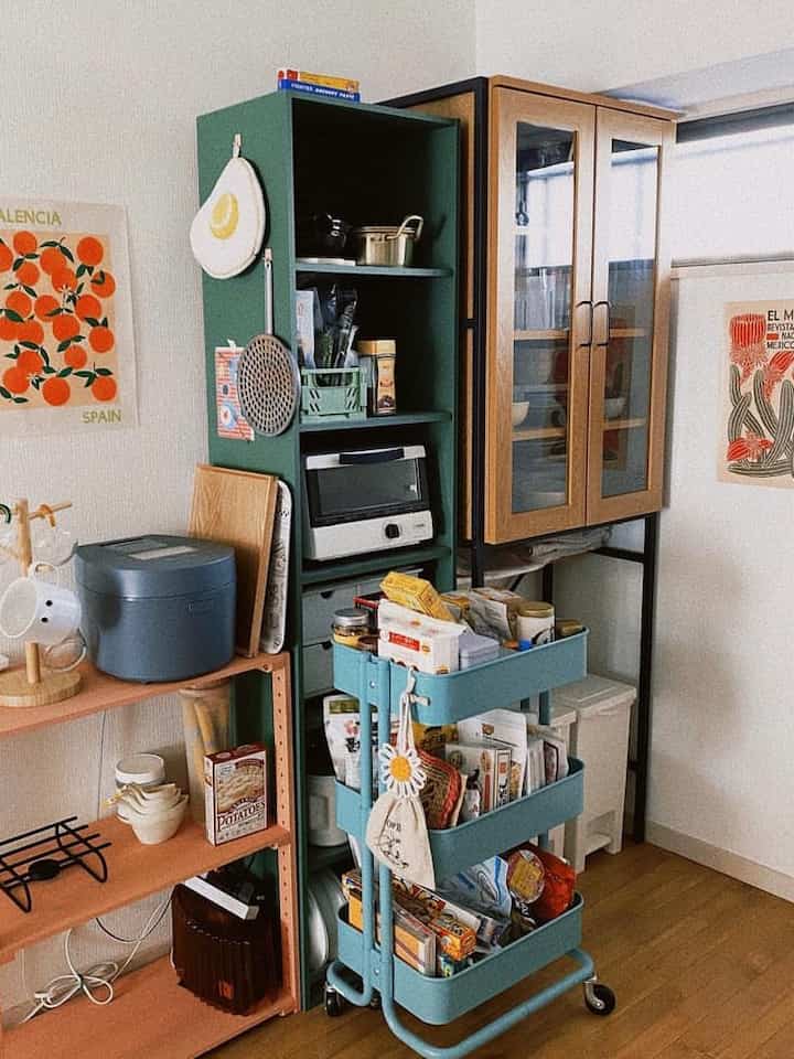Kitchen space featuring green and wood tones, with neatly organized shelves and kitchen cart stocked with various food items and utensils, cozy atmosphere