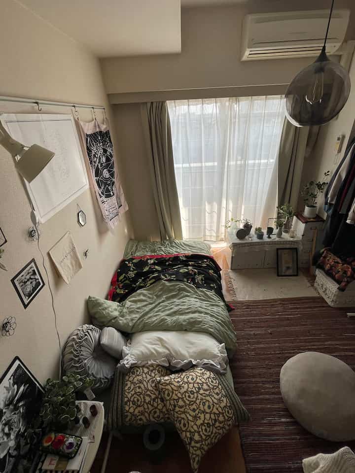 ナチュラルな色調のワンルーム寝室、複数のクッションが置かれた居心地の良い空間