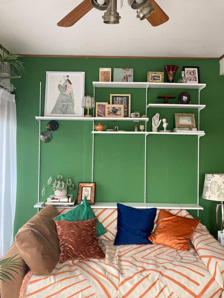Bright green walled living room with orange-striped sofa and velvet cushions creating a cozy atmosphere
