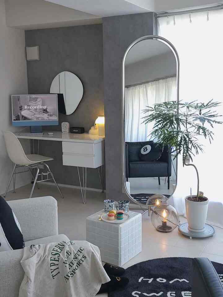 モノトーンとシルバー調のリビング、大きな鏡とアームチェア、デスク、照明が配置された印象的な空間