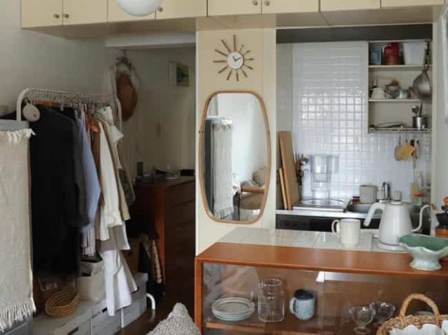 Beige and wood-toned studio kitchen featuring a wall mirror and clothing rack in a cozy single household space