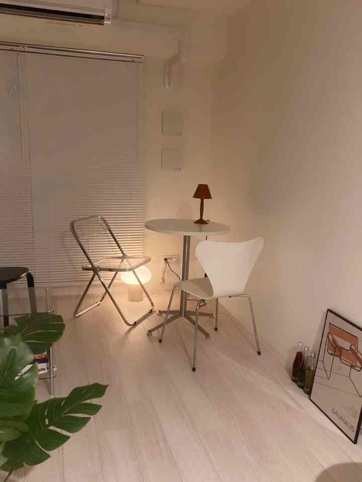 A simple cafe-style living room in white and beige tones featuring a transparent chair and table lamp