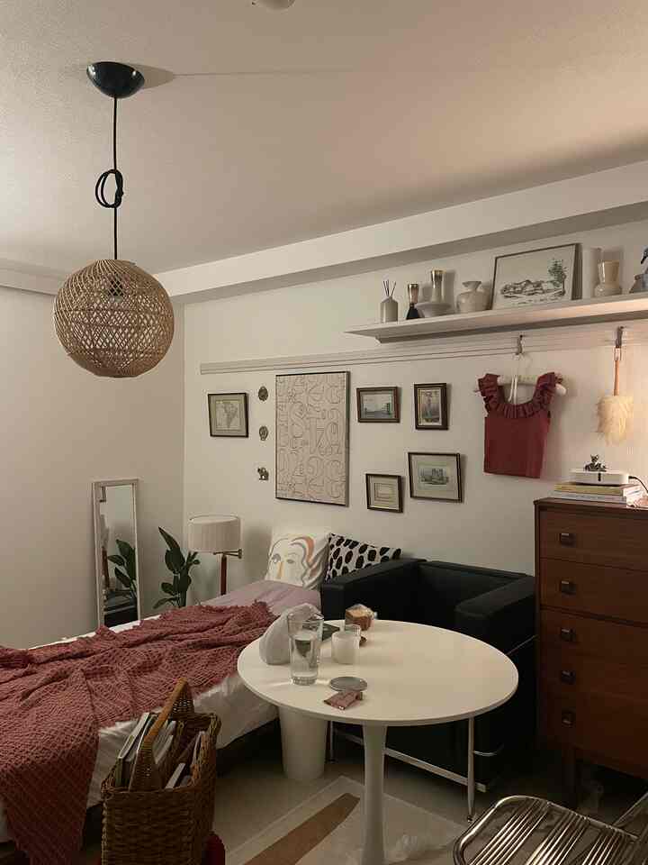 White and brown toned compact studio living room featuring bed, rattan pendant lamp, and gallery wall with cozy atmosphere