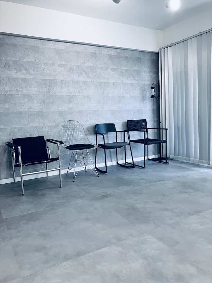 グレーの壁と床に、異なるスタイルの黒とシルバーのダイニングチェアが並べられたモノトーンのダイニングルームのインテリア