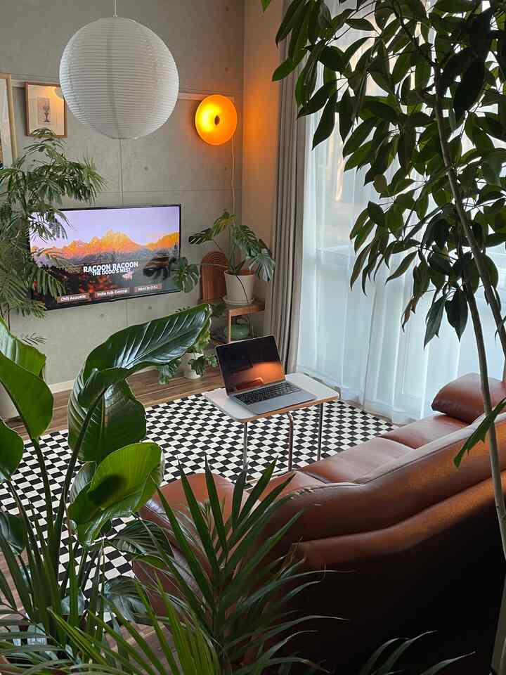 Natural brown sofa with black and white checkered rug in living room featuring abundant plants and warm ambiance