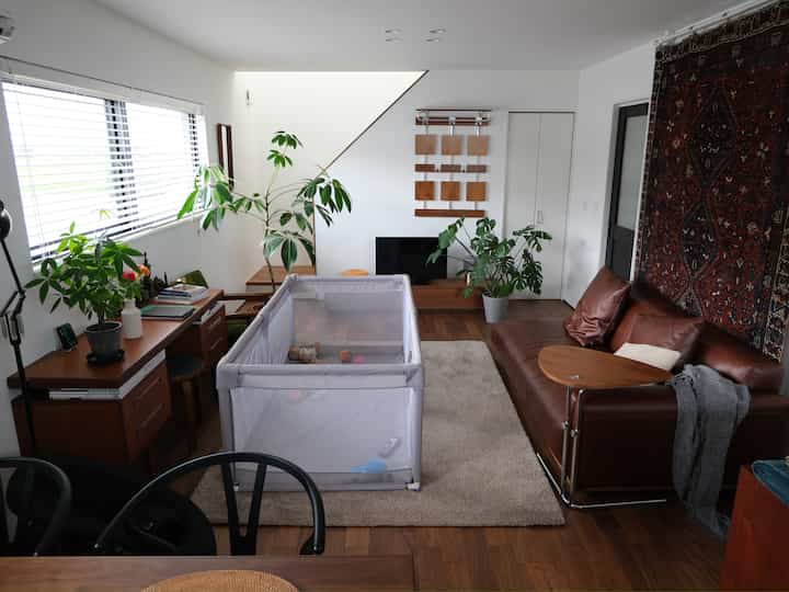 ナチュラルな雰囲気のリビング、中央にベビーサークルとブラウンのソファが配置された印象的な空間