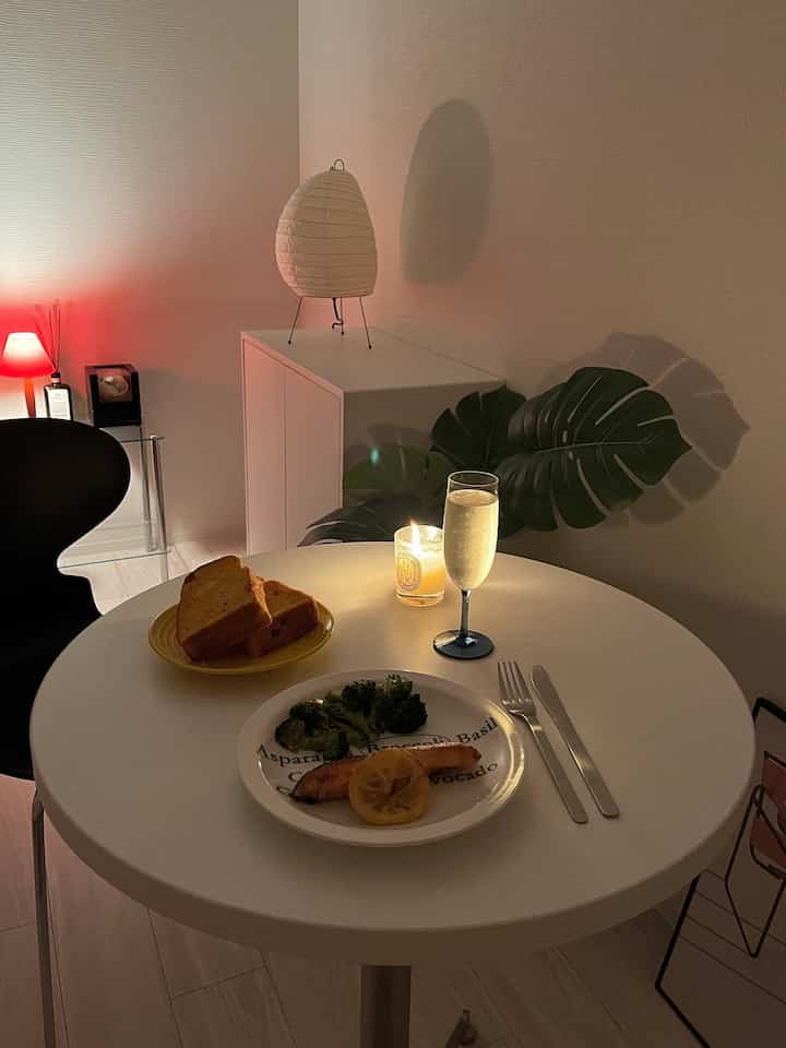 白を基調とした小さな部屋、すっきりとしたダイニングテーブルと植物、柔らかな照明が配置された雰囲気のあるおうちカフェ空間