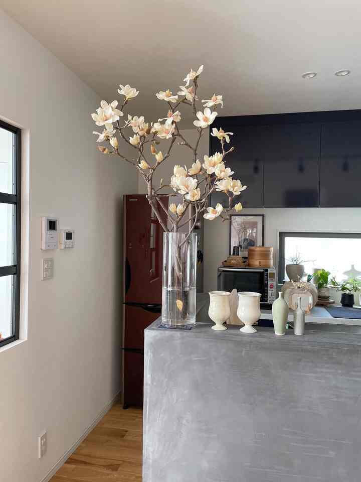 白い壁とナチュラルな木目調の床があるキッチン、透明な花瓶にクリーム色の花が配置されたシンプルな雰囲気のインテリア