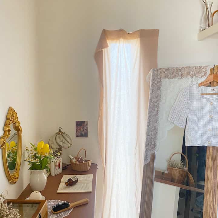 White and beige toned walk-in closet featuring gold-framed mirror, wooden furniture, and wicker baskets in a natural setting