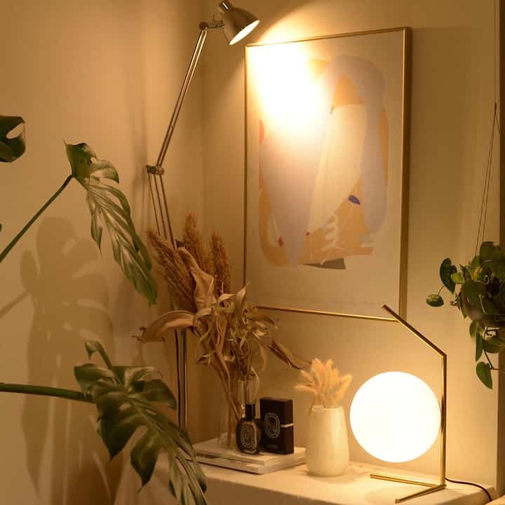 温かみのあるベージュ調の室内コーナー、ゴールドアクセントの照明と花瓶が落ち着いたリビングの雰囲気を演出