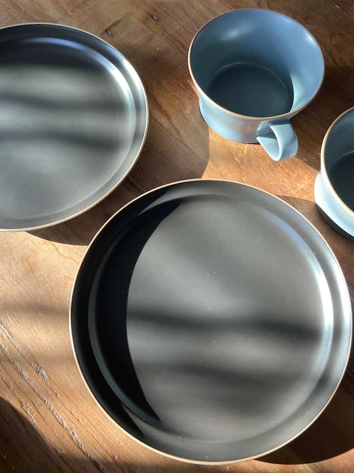 ナチュラルな木目調のダイニングテーブルに配置されたグレーの皿とパステルブルーのスープカップが並ぶ清潔感のあるダイニング空間