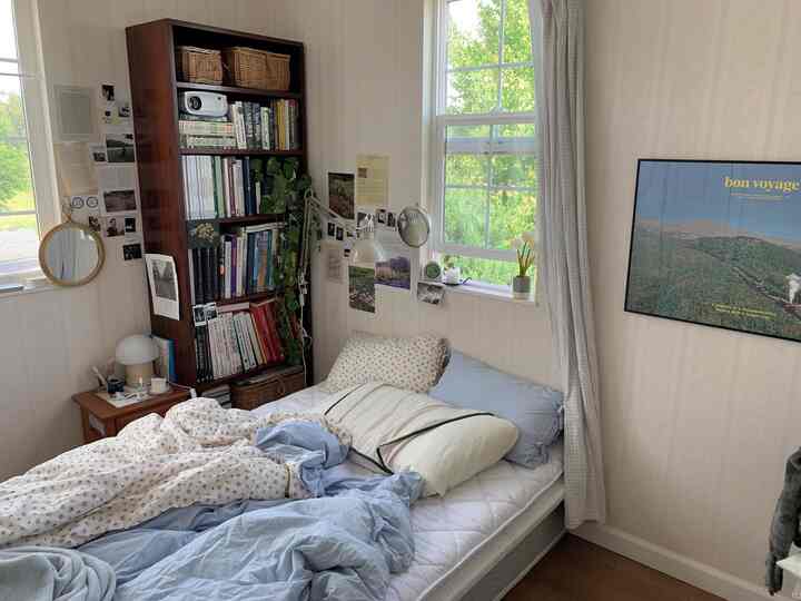 ホワイトとブルーの色調が特徴的な6畳の寝室で、ベッドと本棚が配置されたナチュラルで北欧風の雰囲気のあるインテリア