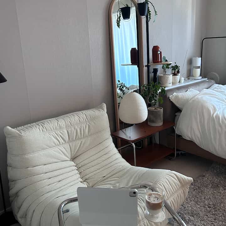 アイボリーのソファとナチュラルな木製棚、ベッドが配置されたシンプルで自然な雰囲気の寝室