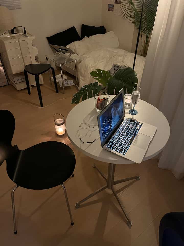 Natural tone single household bedroom featuring a round table with laptop and candles, creating a cozy nighttime atmosphere