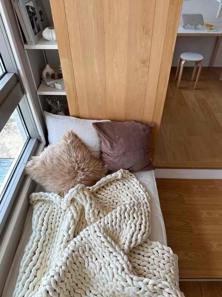 ナチュラルカラーの寝室、ふんわりとしたニットのブランケットとクッションが並び、片隅にはホームオフィス用のデスクとスツールが配置された雰囲気のあるインテリア。