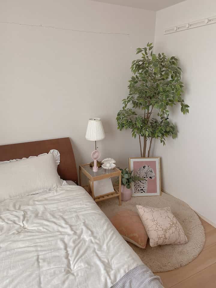 Natural-toned bedroom featuring a wooden nightstand, white table lamp, and artificial green plant creating a soft atmosphere
