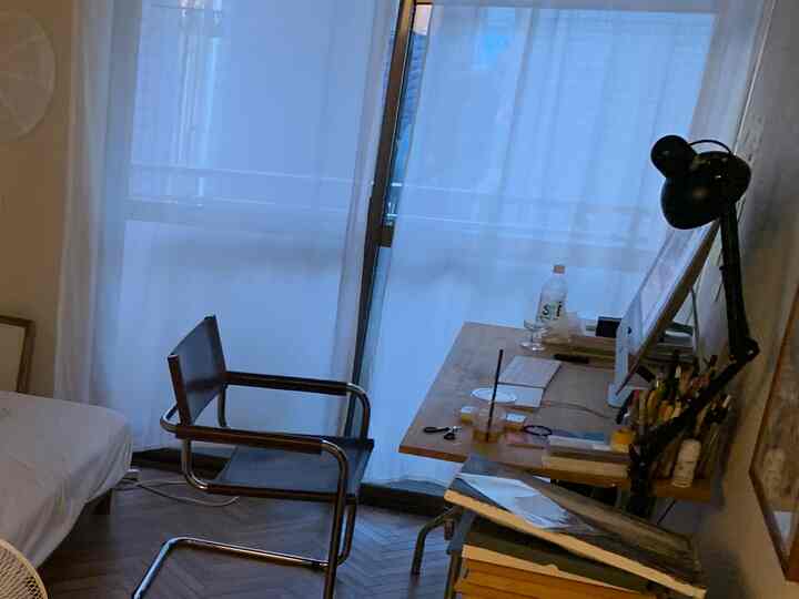 白いカーテンと茶色のデスクが配置された、一人暮らし向けの小さくて居心地の良い寝室兼ホームオフィス