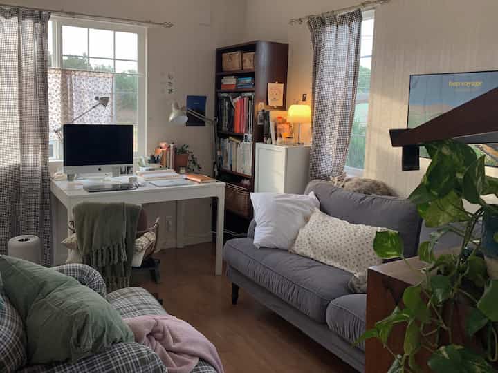 グレーとブラウンの色調が特徴のリビング、白いデスクとソファ、猫がいる温かみのあるナチュラルスタイルの空間