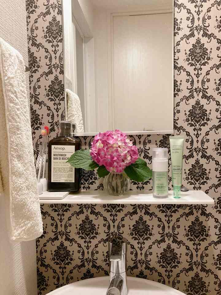 ナチュラルな色調のパウダールーム、洗面台の上にトレイとピンクの花瓶が置かれた印象的な空間