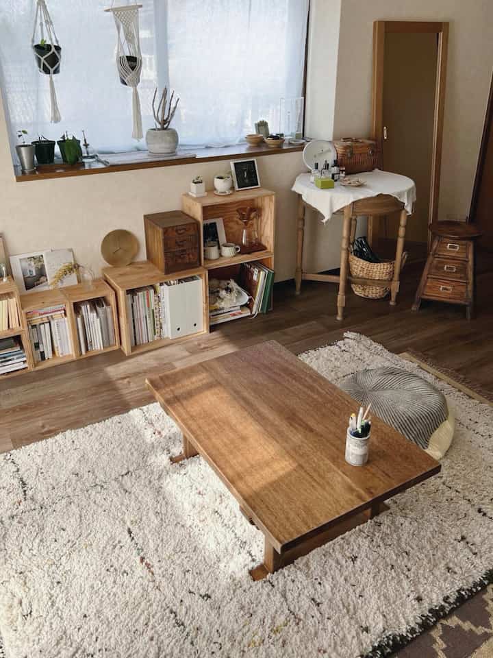 ライトブラウンの木目調とオレンジ色の光が溢れるリビング、低い木製テーブルと棚、クッションが置かれた自然な雰囲気のインテリア