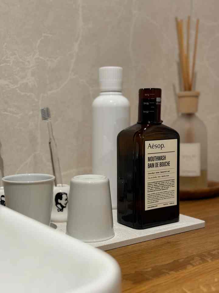 白と木目調が調和したバスルームの洗面台に、イソップのマウスウォッシュと歯ブラシ、ディフューザーが配置された印象的なインテリア