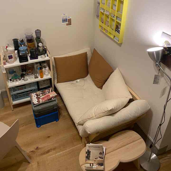 木目調と白を基調としたコンパクトなワンルームリビング、ソファベッドとコーヒーテーブル、フロアランプが配置された雰囲気のあるインテリア