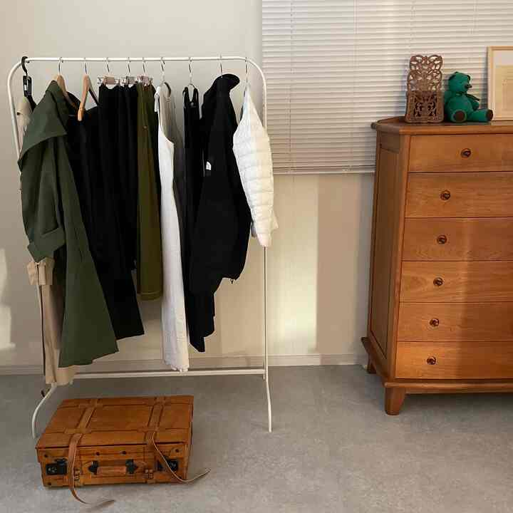 白を基調とした壁に洋服ラックとブラウンの木製チェストが配置された落ち着いた雰囲気のウォークインクローゼット