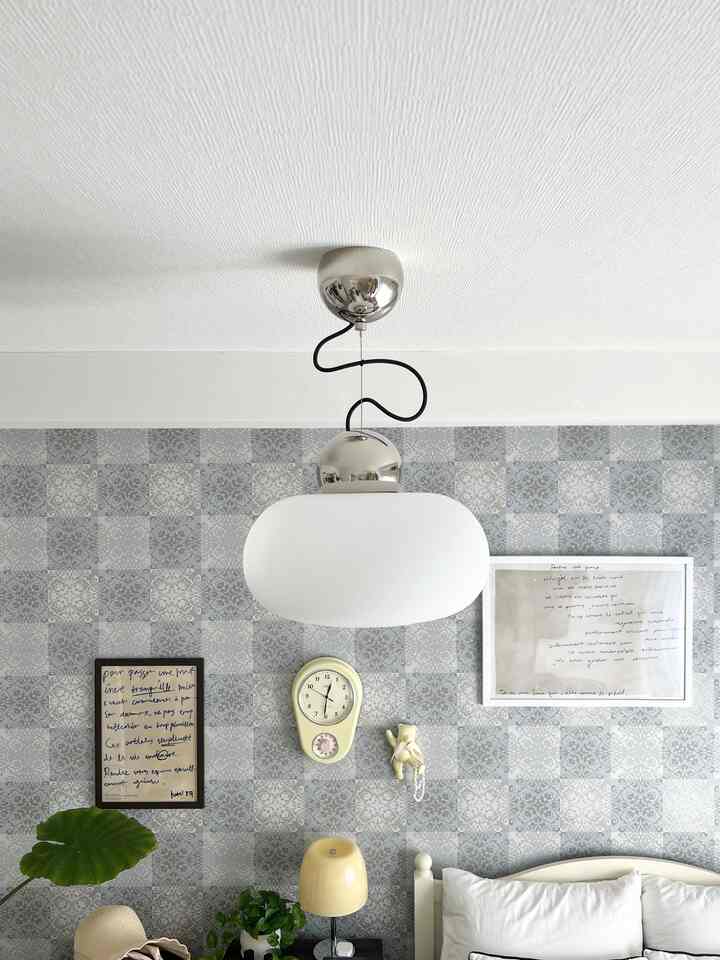 Natural-toned bedroom with gray patterned wallpaper and white bed, featuring a large white pendant light centrally hung from the ceiling