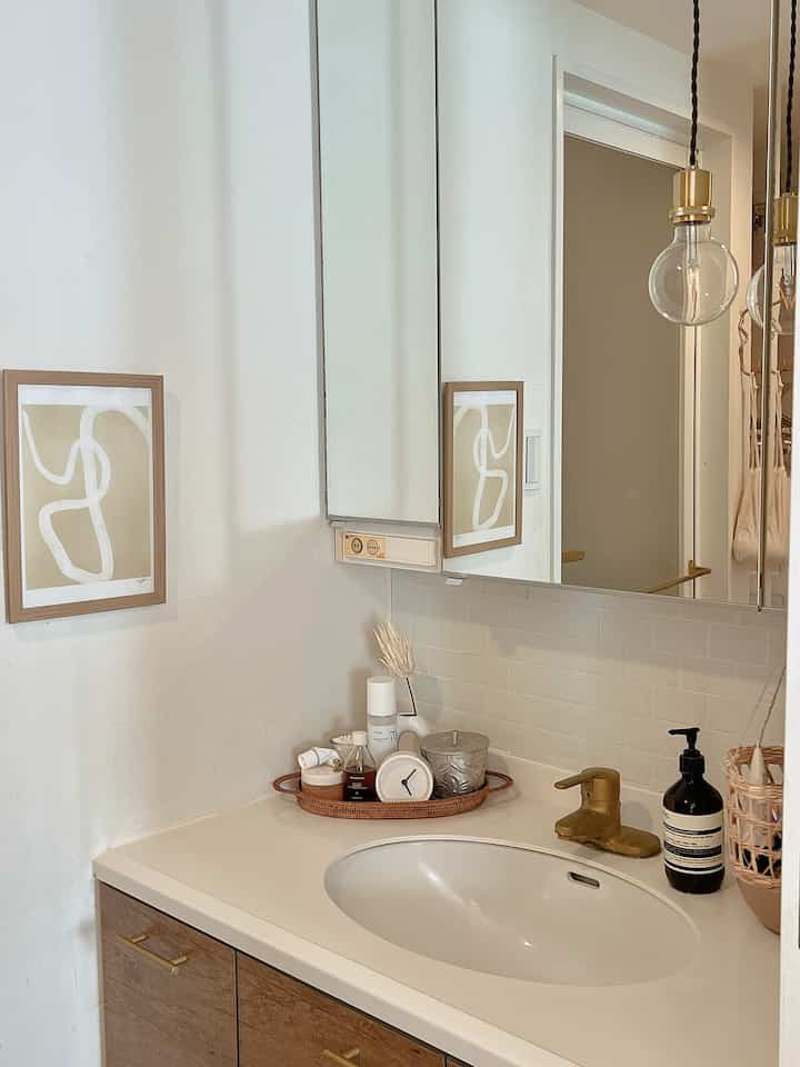 白と木目調が調和したバスルームの化粧台、大きな鏡とゴールドの水栓が配置されたモダンな空間