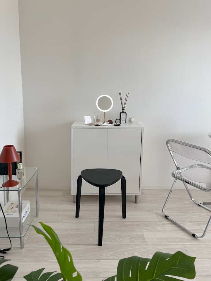 White and black toned living space featuring a white cabinet with a black stool and a round LED travel mirror on top, creating a neat atmosphere