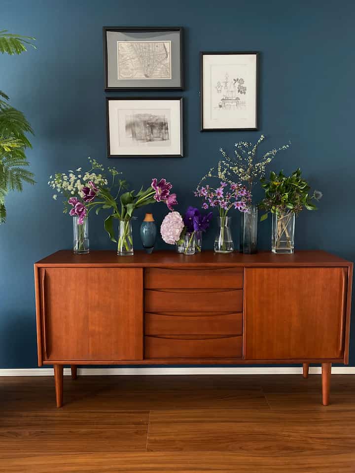 深い青色の壁に置かれた茶色のサイドボードと透明な花瓶が飾られた洗練されたインテリア空間