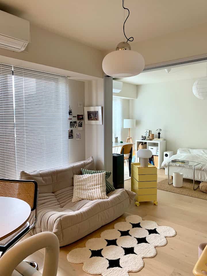 Natural color toned 2K apartment living room connected to bedroom with sofa, cushions, and yellow storage unit, clean and cozy interior