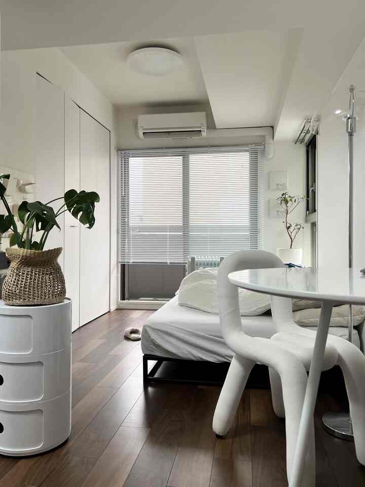 白と木目調の調和が美しいワンルームの寝室、ダイニングテーブルと植物が配置されたシンプルで落ち着いたインテリア