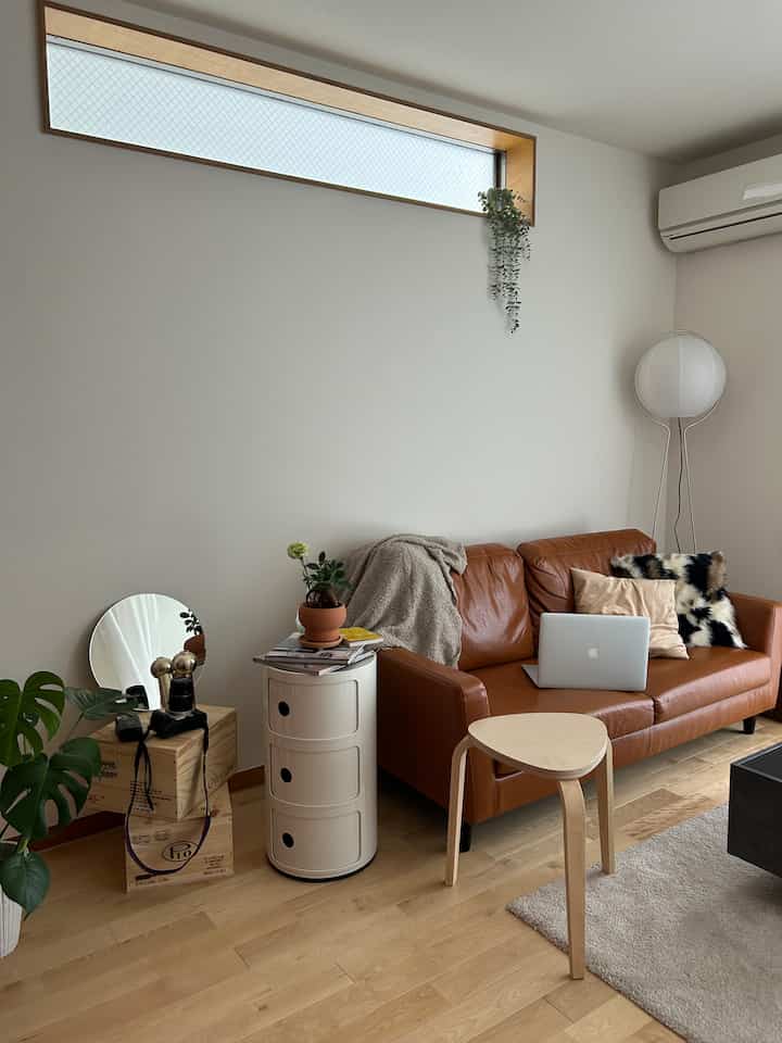 Bright white wall and wood-toned floor living room featuring brown leather sofa and simple wooden stool in a natural modern style space