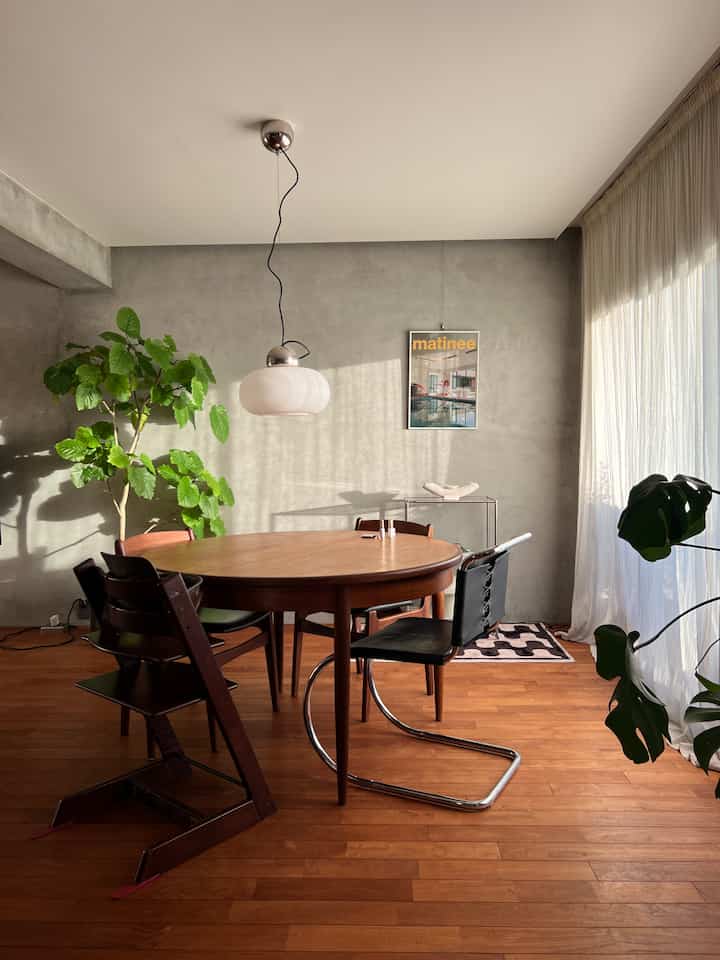 ウッドトーンとグレーの壁のダイニング空間、丸テーブルとヴィンテージチェア、ペンダントライトが配置されたミッドセンチュリーモダンヴィンテージの雰囲気あるインテリア
