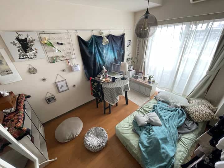 ナチュラルな色調の小さな一人暮らしの部屋、ベッドとホームオフィス用テーブルが配置された印象的な空間